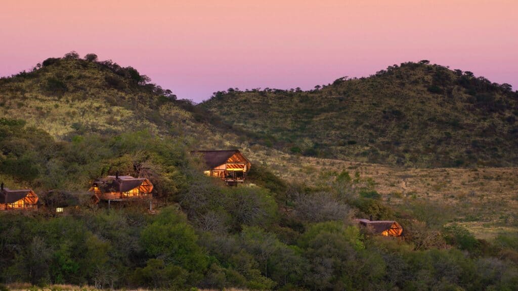 Scenic view of safari lodges in Pilanesberg at sunset with lush greenery and rolling hills.